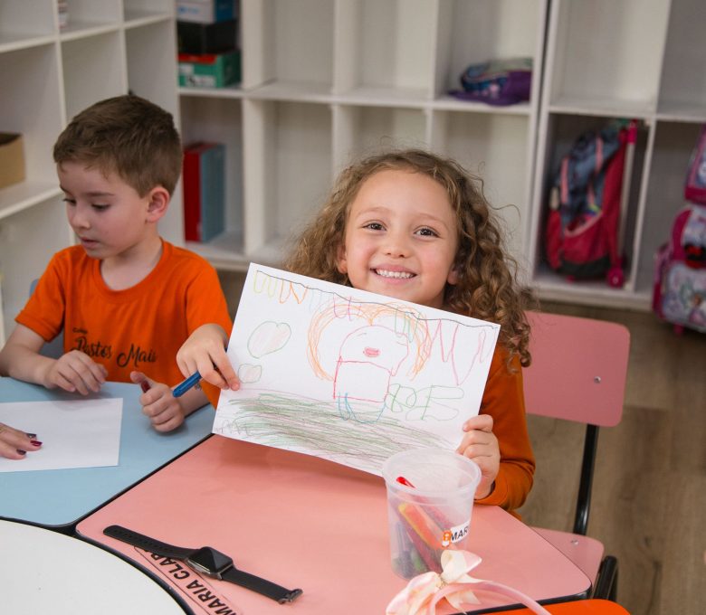 Criança mostra desenho em giz de cera feito na sala de aula - Escola Bem Melhor